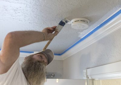 A man paint the ceiling around smoke detector